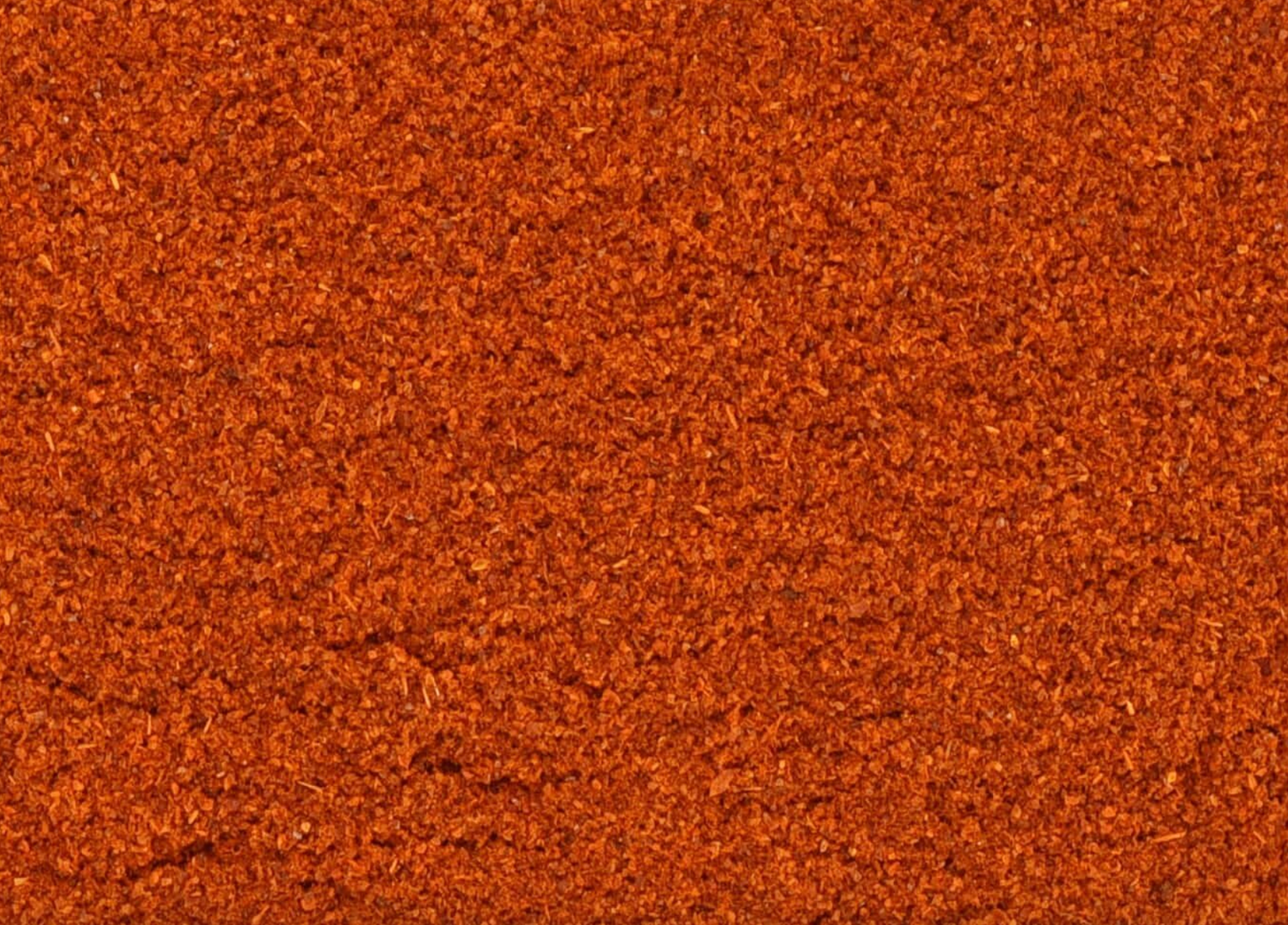 Close-up of texture of dried cayenne pepper powder, vibrant red and finely ground, used for teas and herbal remedies.
