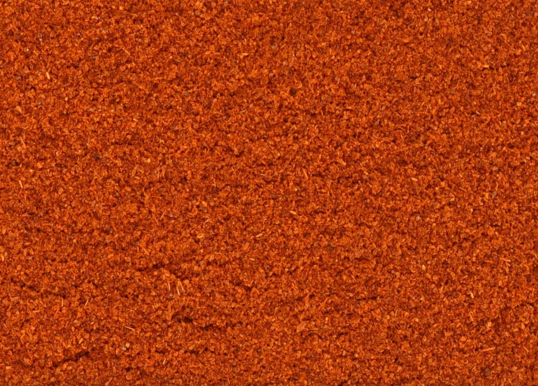 Close-up of texture of dried cayenne pepper powder, vibrant red and finely ground, used for teas and herbal remedies.